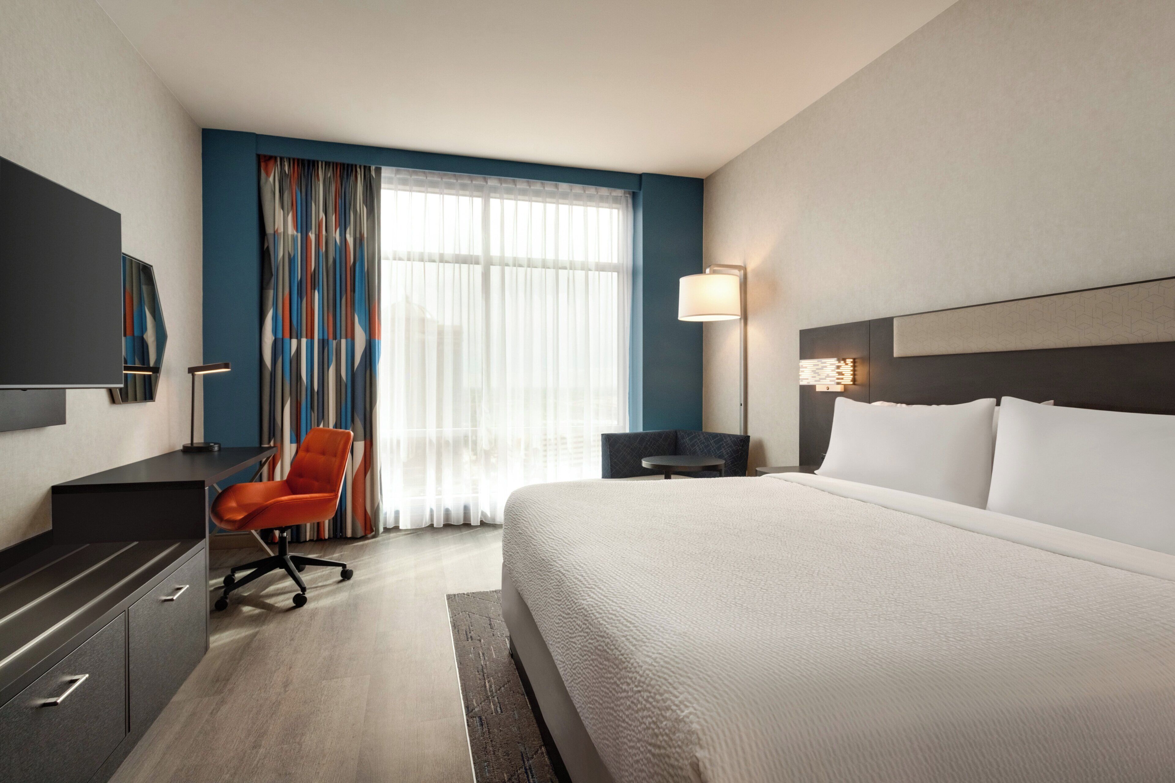 A hotel room with a large bed, a desk with a chair, a TV, and a window with curtains.