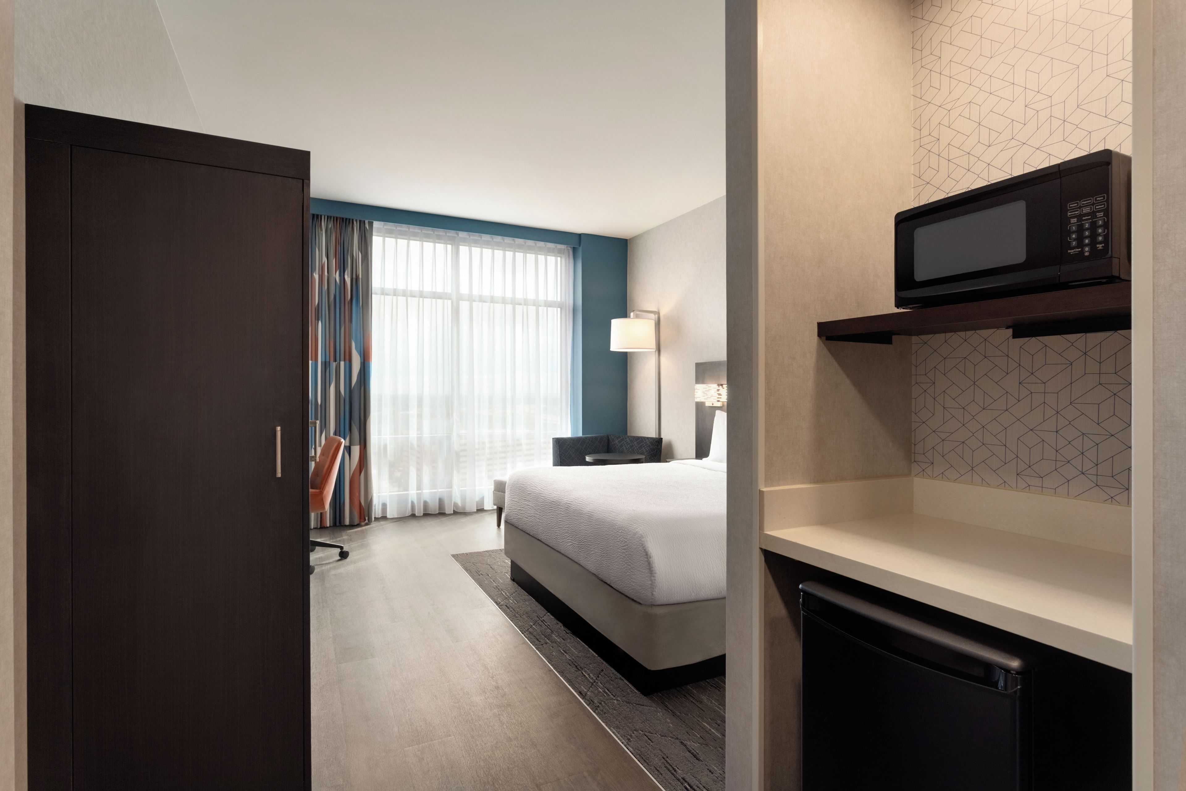 Una habitación de hotel con cama, escritorio, microondas y armario.