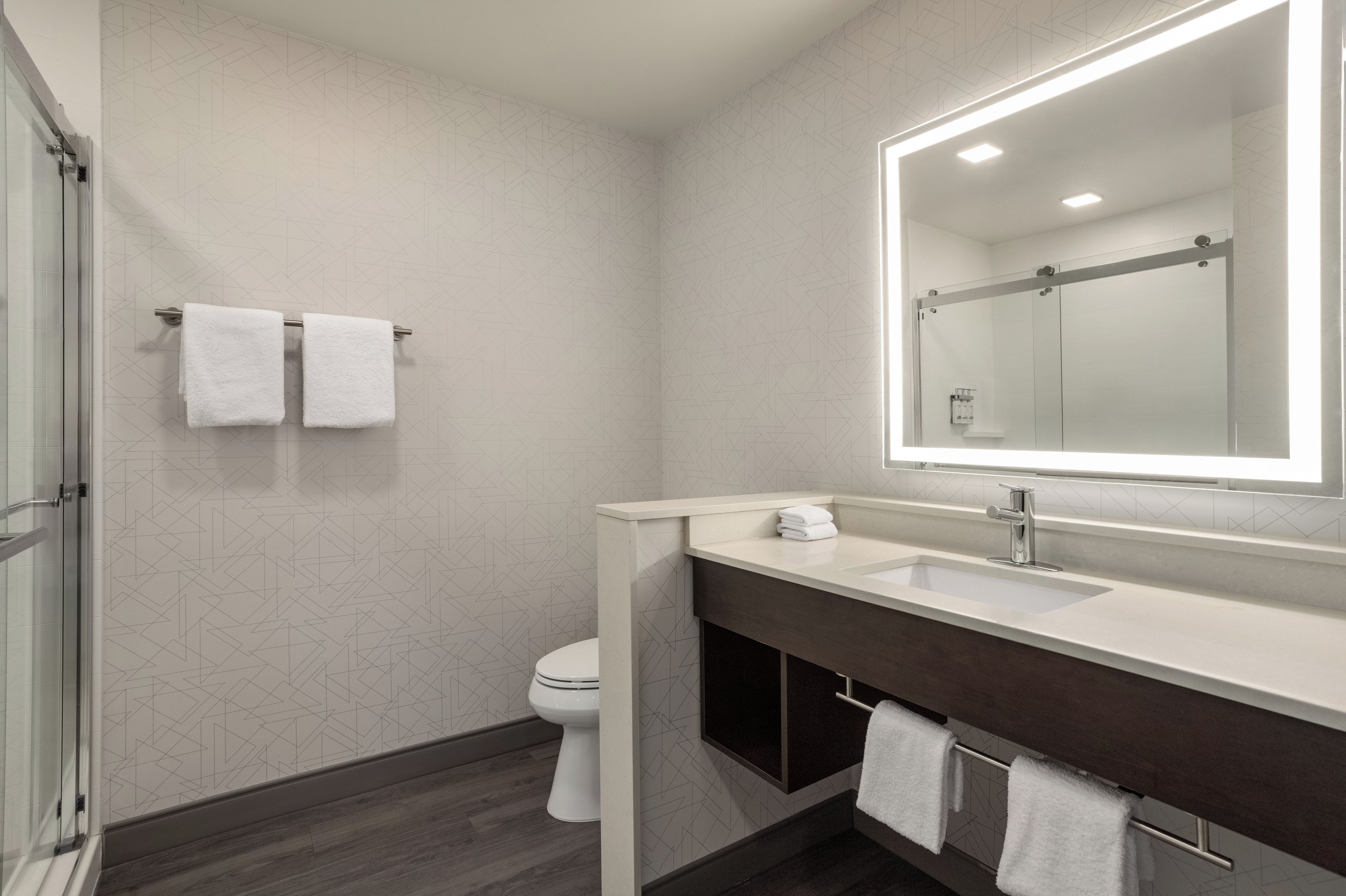 A modern bathroom with a glass shower enclosure, a white toilet, a vanity with a mirror, and two towels hanging on the wall.