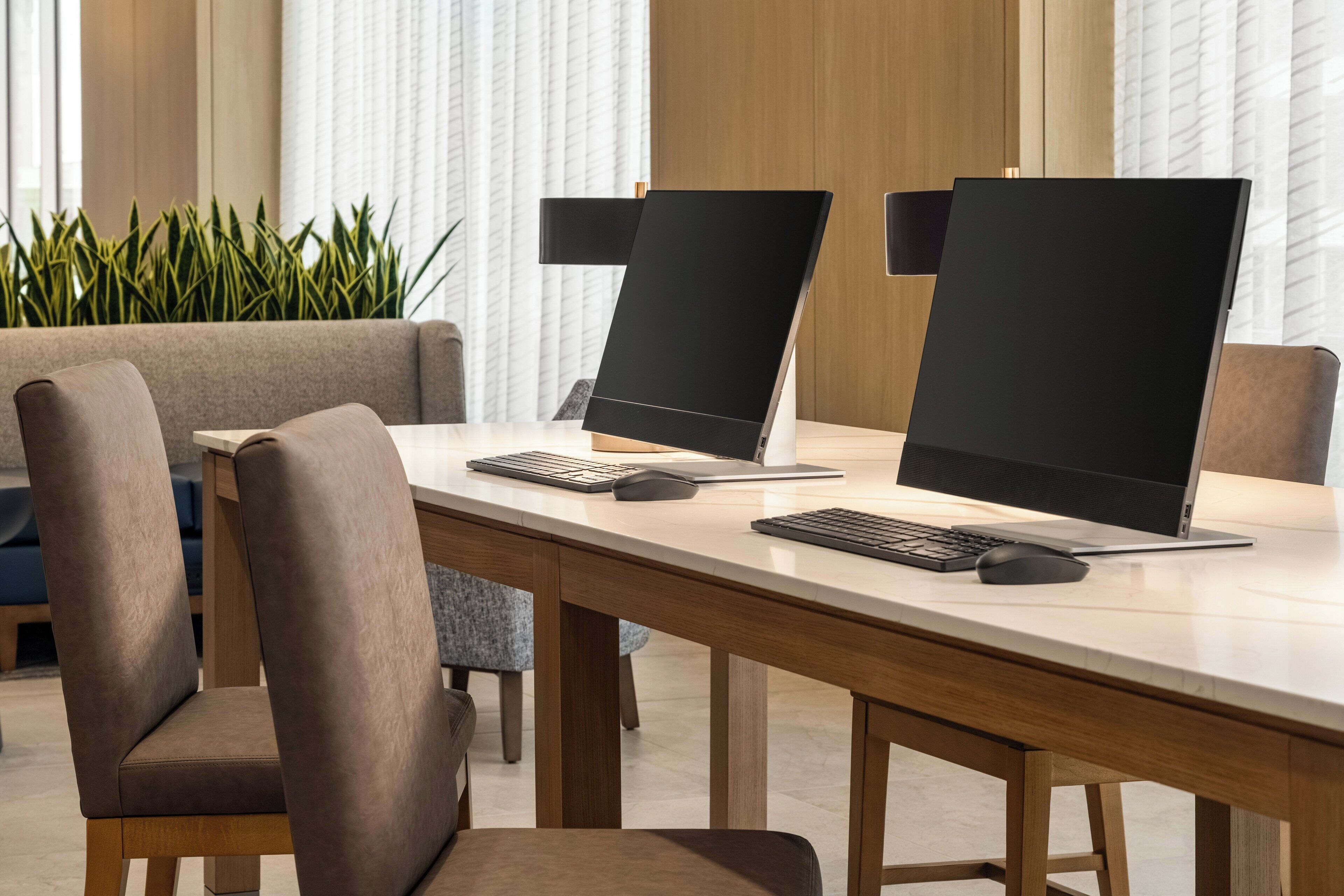 A modern office space with two laptops on a wooden desk, surrounded by chairs.