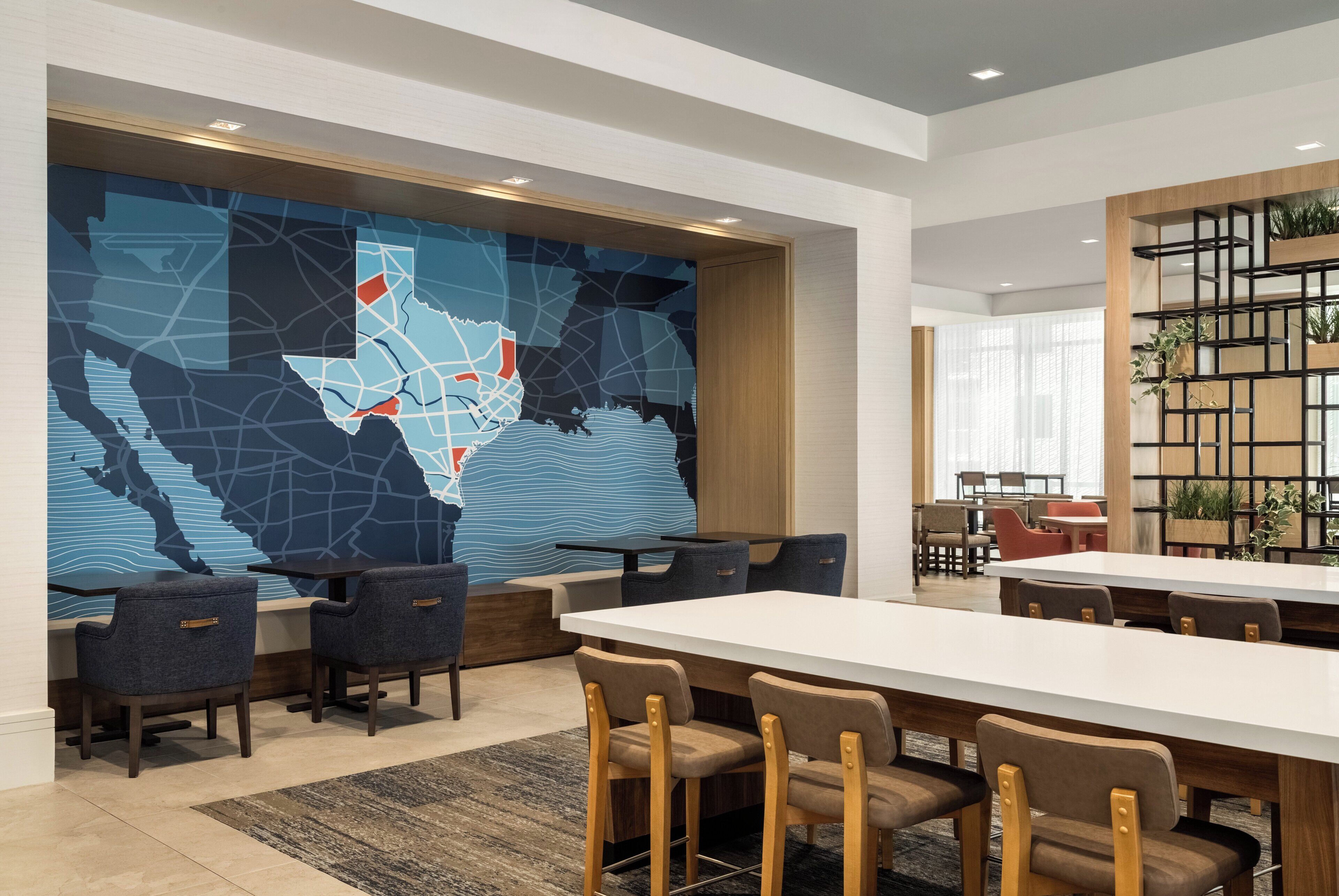 A modern dining area with a large table and chairs, a map mural on the wall, and a plant shelf.