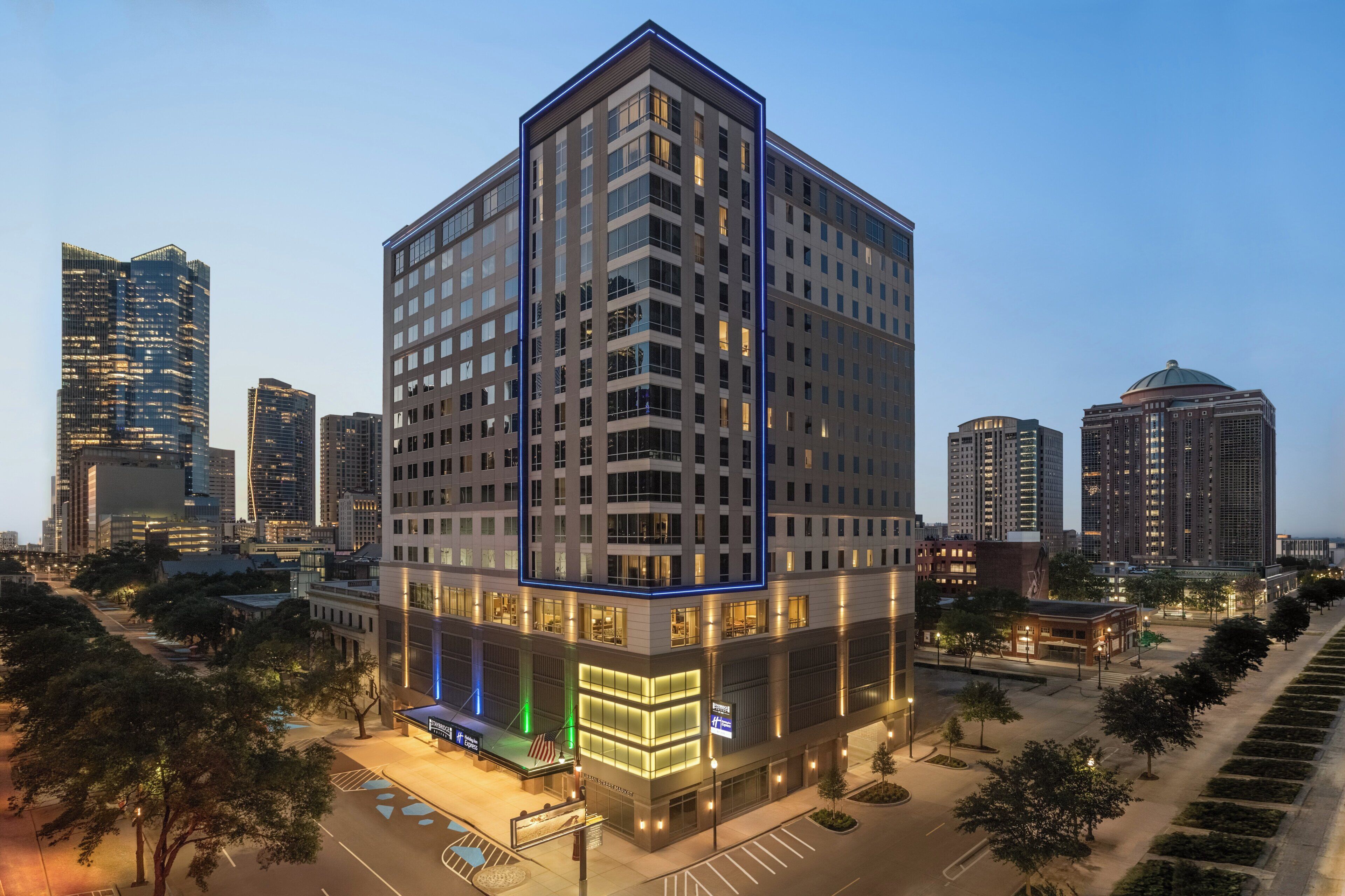 A multi-story hotel with a modern design, featuring a prominent corner entrance and a visible parking area.