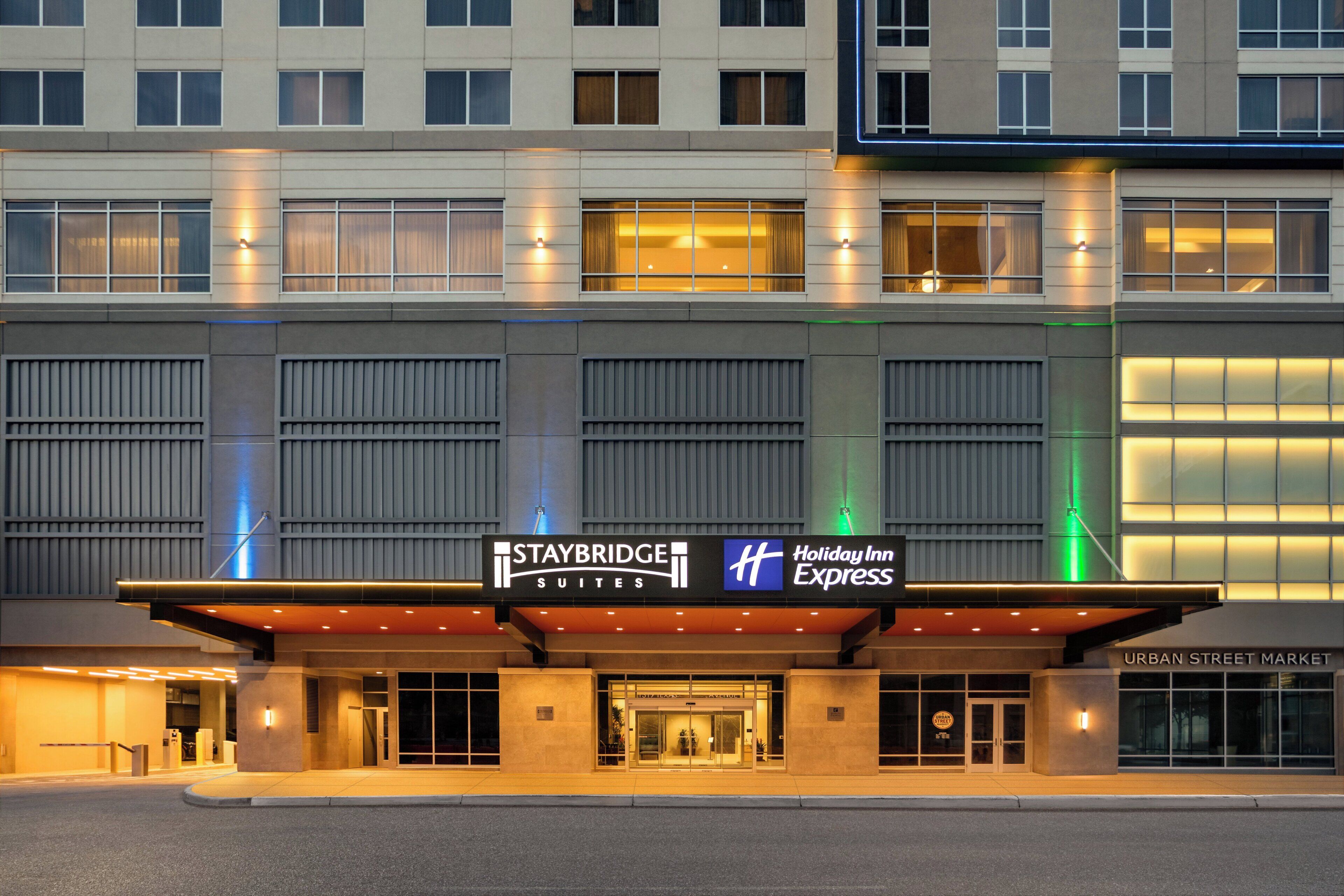 Un hotel Staybridge Suites con la marca Holiday Inn Express, que presenta una fachada moderna con amplios ventanales y una entrada destacada.