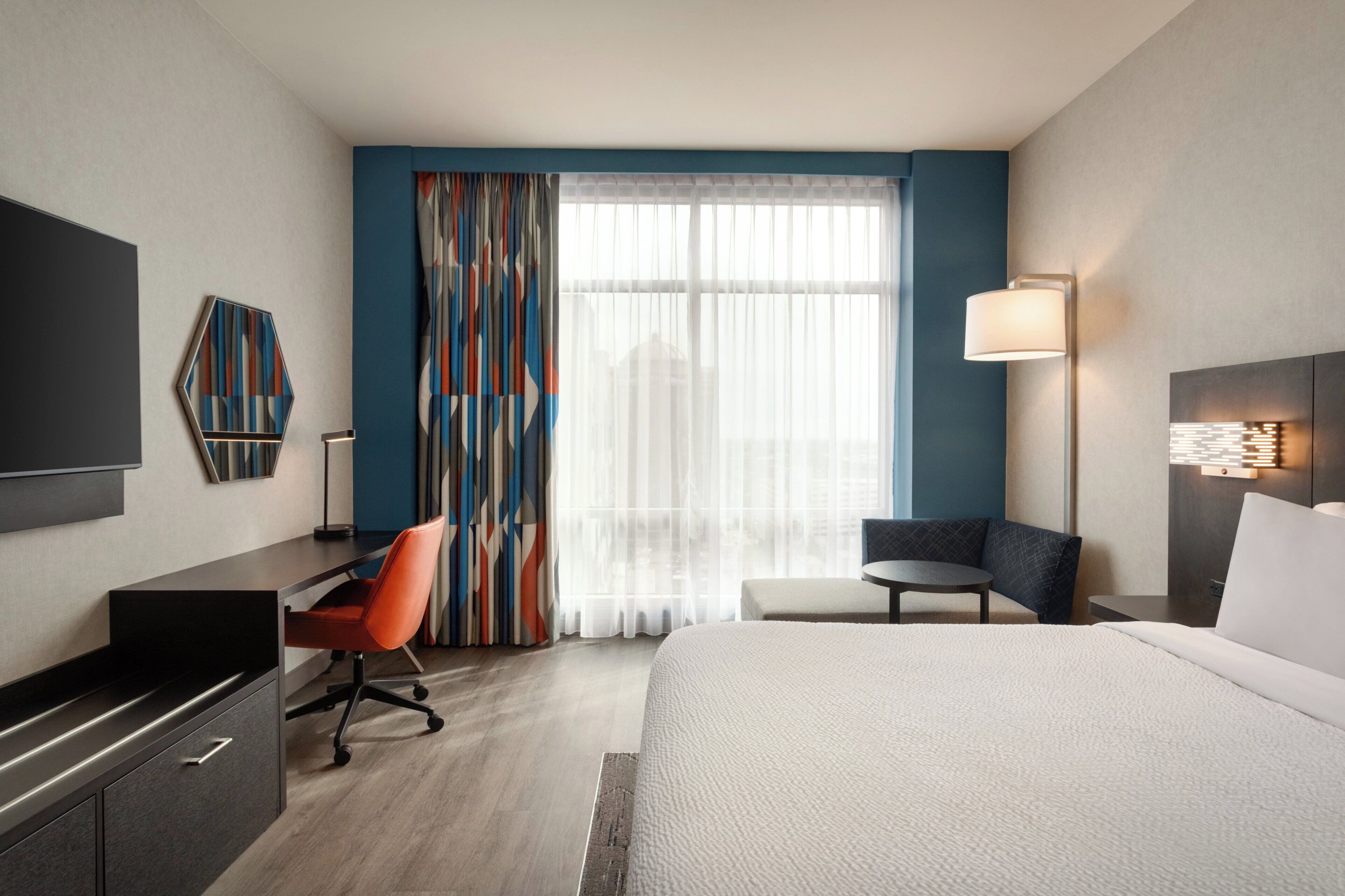A hotel room with a bed, a desk, a chair, a television, and a window with curtains.