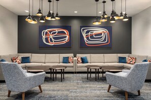 A modern lounge area with a sofa, two armchairs, and a coffee table. There are abstract paintings on the wall and pendant lights above. - Holiday Inn Express Houston Downtown by IHG (Houston)