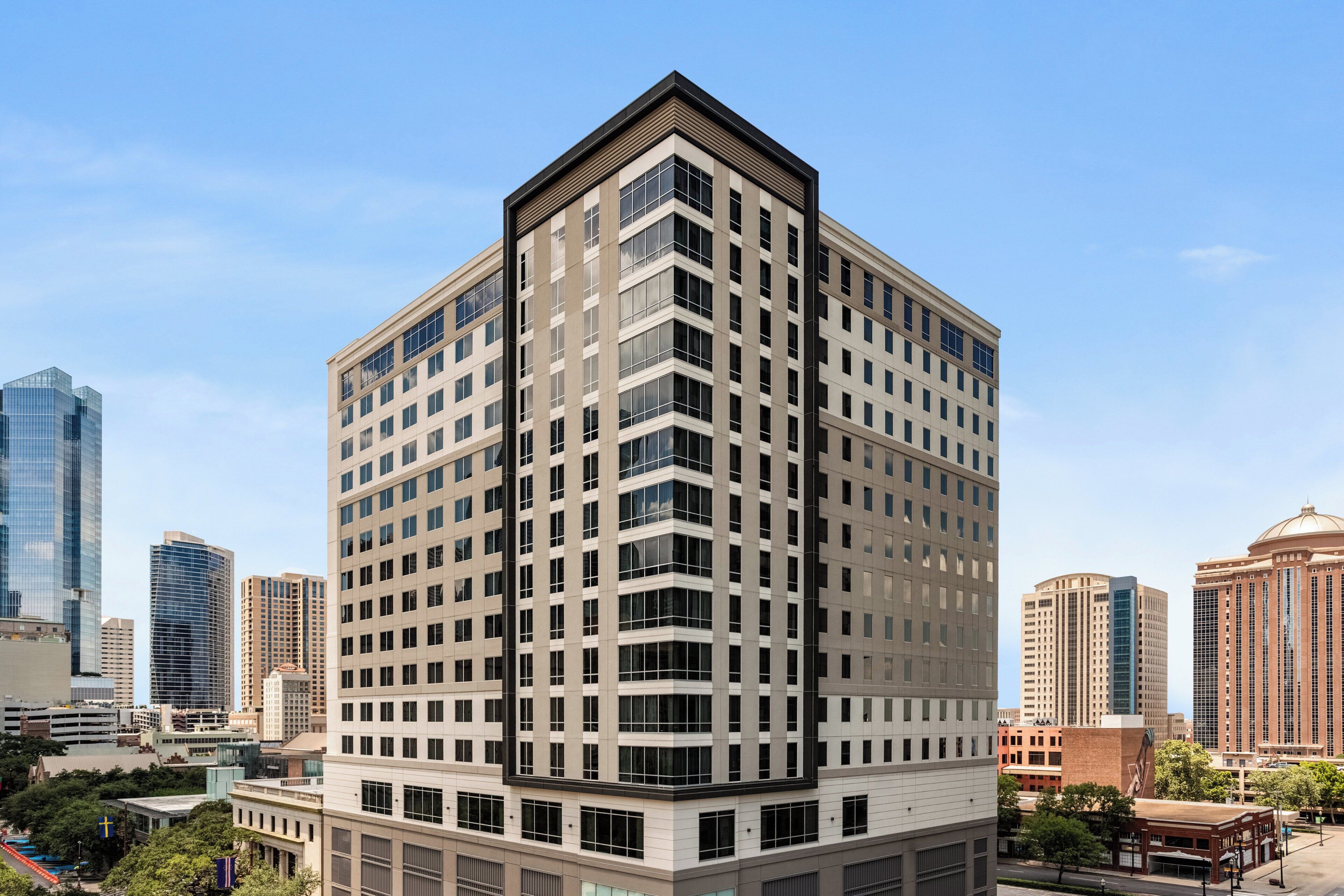 A multi-story hotel with a modern design, featuring a prominent corner entrance and a large glass facade.