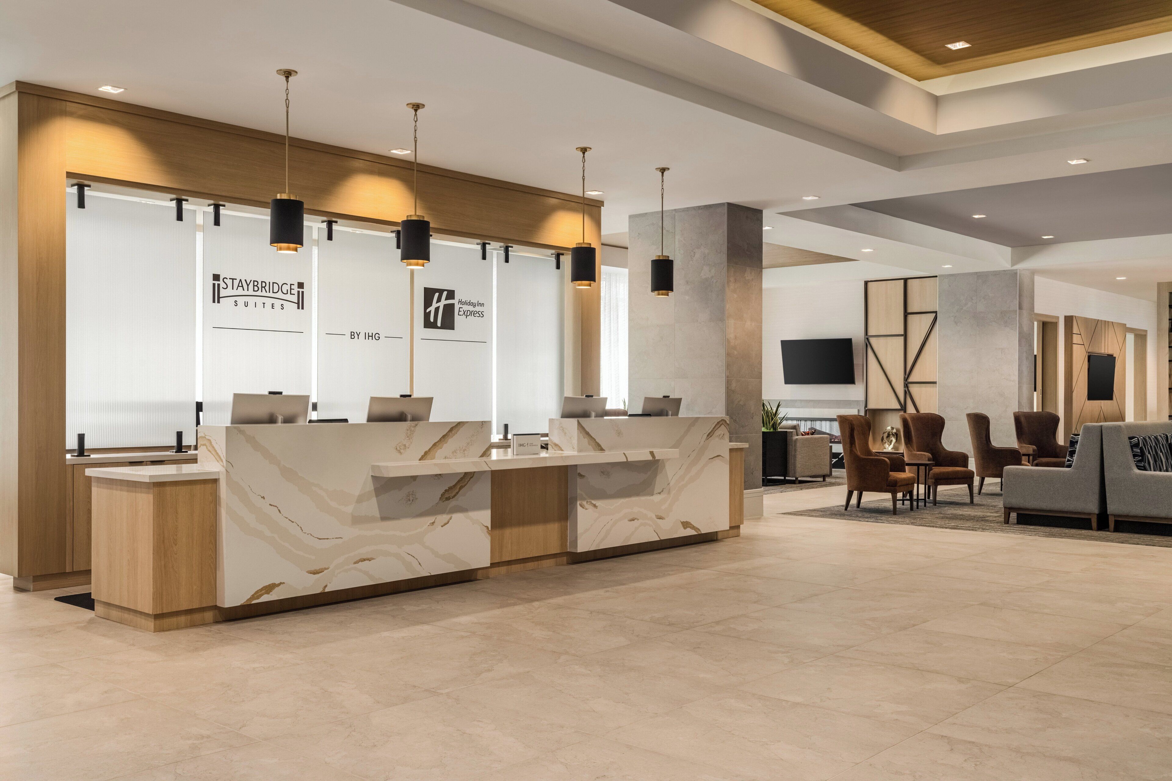 A hotel reception area with a marble reception desk, a seating area with sofas and chairs, and a flat-screen TV mounted on the wall.