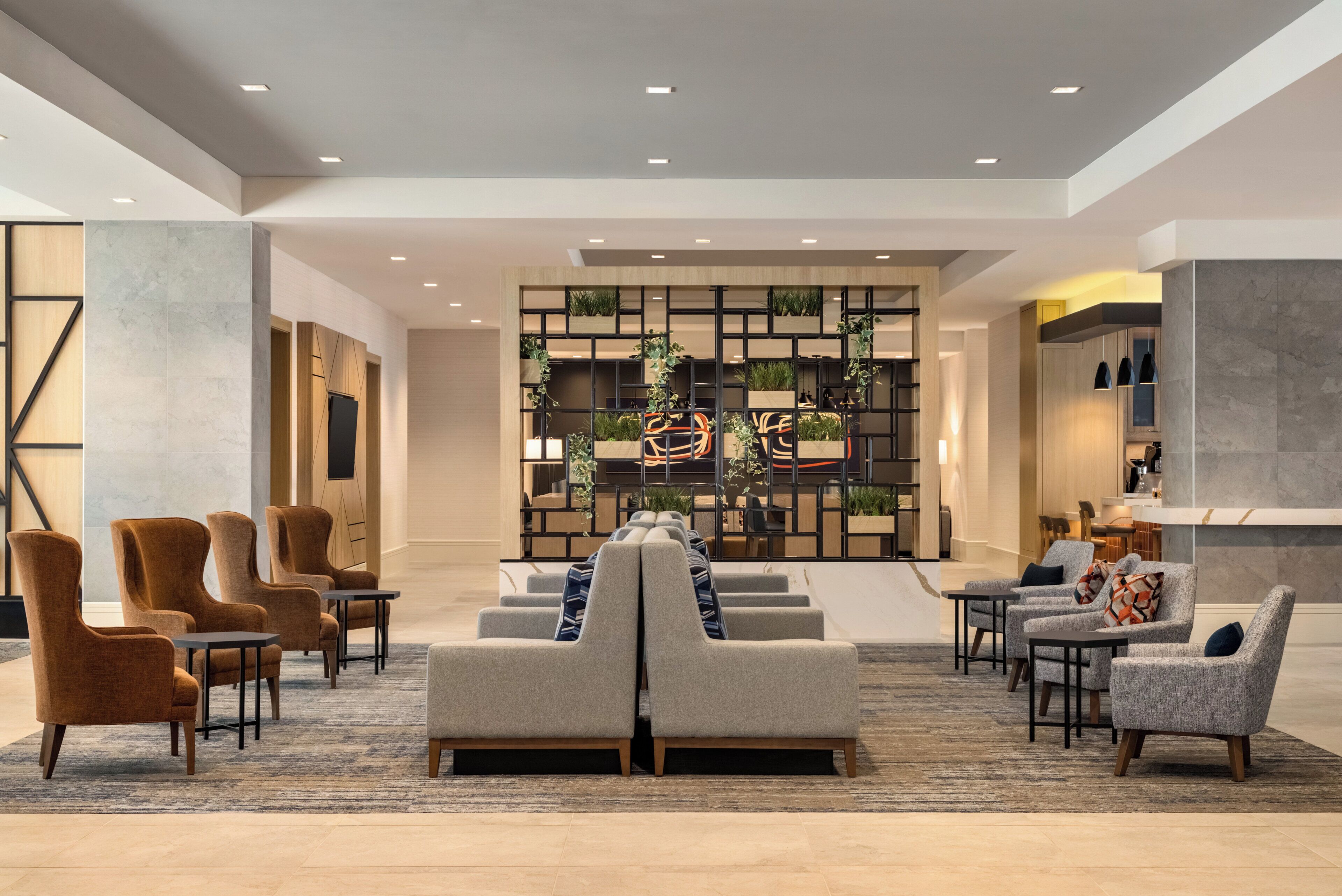 A modern lobby with seating areas, a reception desk, and a decorative wall with plants.
