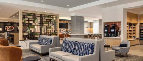 A modern lobby with sofas, armchairs, a bar area, and a kitchen in the background.