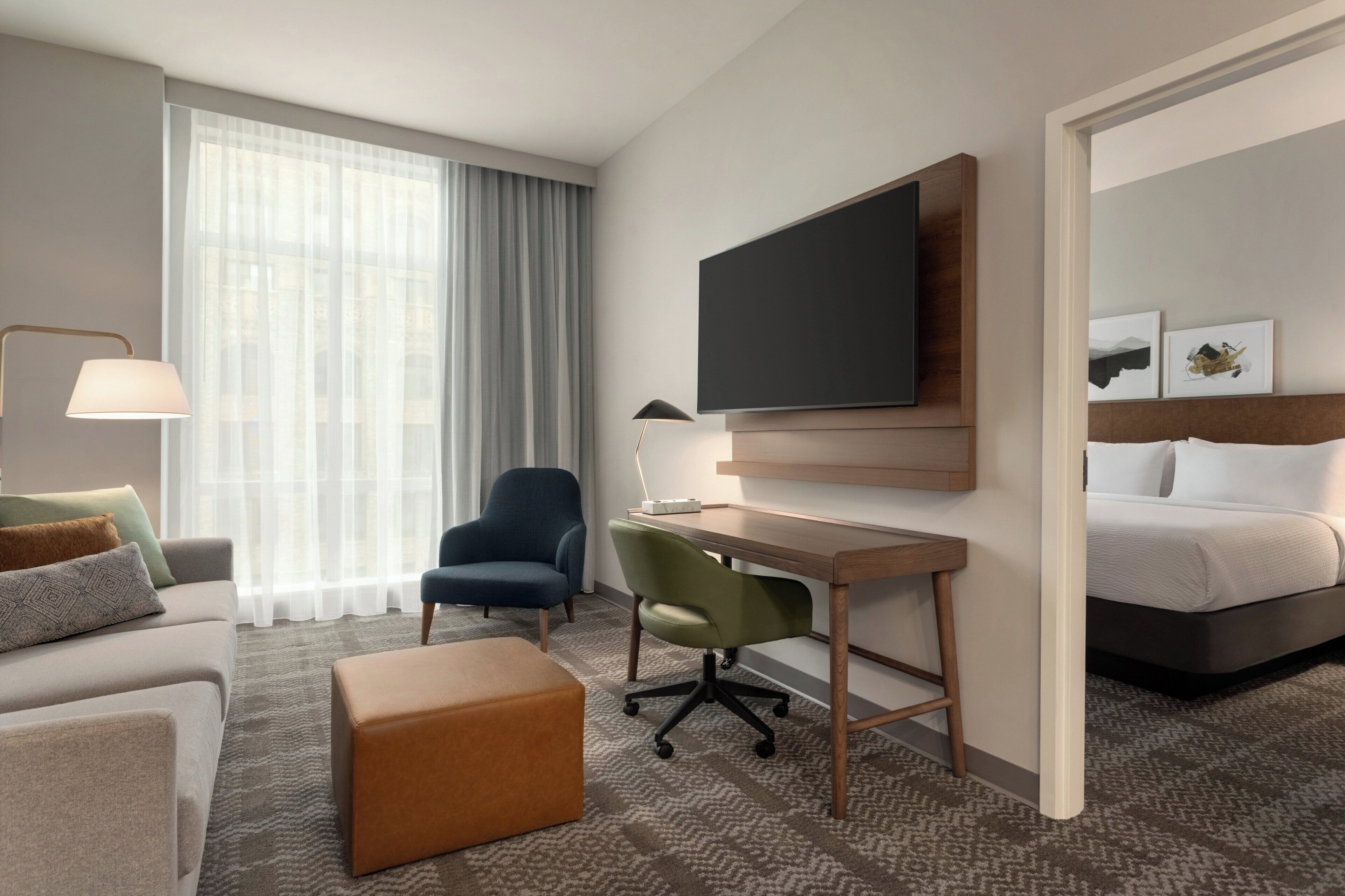 A hotel room with a bed, a desk, a chair, a sofa, a TV, and a window with curtains.