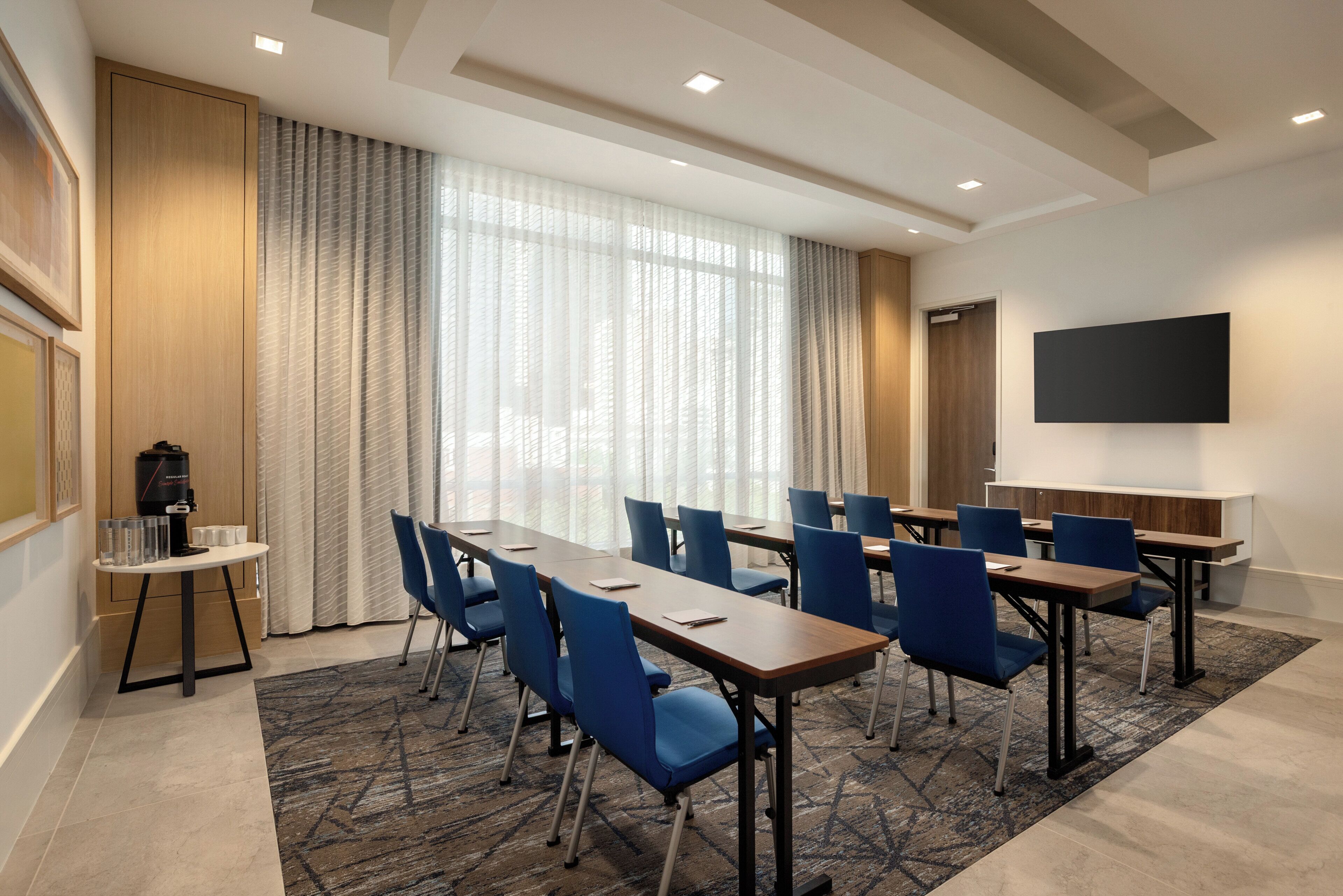 A conference room with a long table, blue chairs, a flat-screen TV, and a coffee machine.
