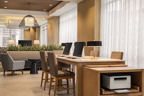 A modern hotel lobby with a reception desk, seating area, and large windows.