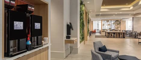 A modern hotel lobby with a coffee station, seating area, and a view of the dining area.