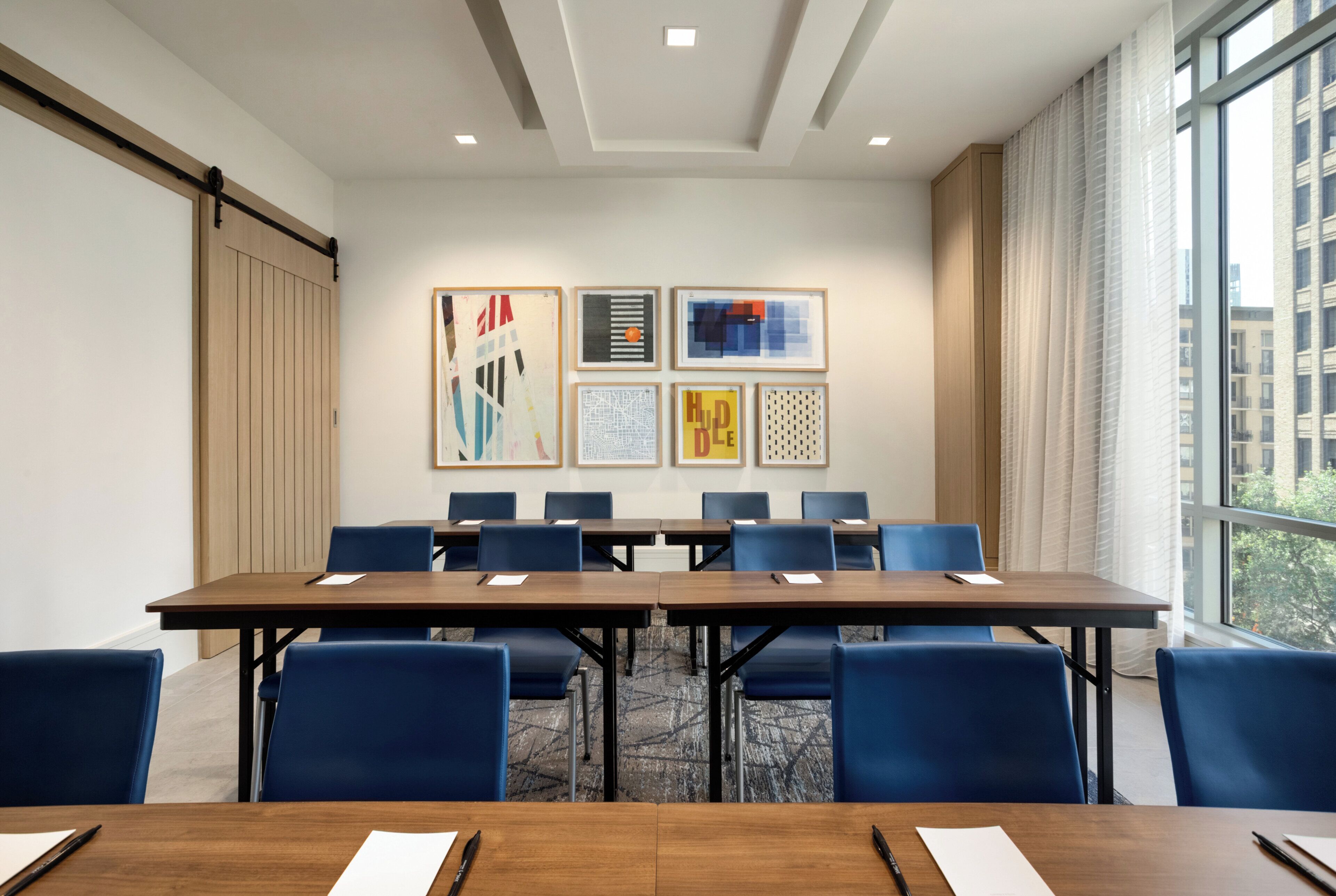 A conference room with a long table, blue chairs, and framed artwork on the wall.