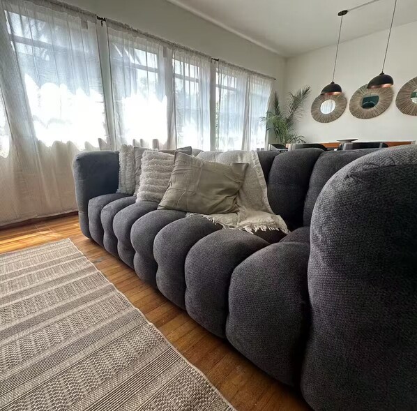 A modern living room with a dark grey sofa, a patterned rug, and a large window with sheer curtains.