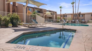 Un espace piscine aménagé avec des chaises longues, des parasols et un bâtiment à la façade beige.
