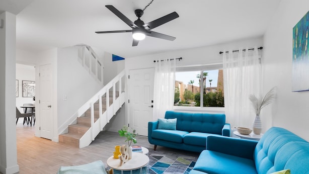 Un salon moderne avec un canapé bleu, une table basse ronde et un escalier menant à une autre pièce.