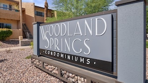Une enseigne pour le complexe résidentiel Woodland Springs, au design moderne, offrant une vue dégagée sur l’entrée du bâtiment et intégrant un palmier en arrière-plan.