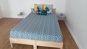 A bedroom with a wooden bed, a round mirror, a wall art piece, and a small side table. - Large Studio in quiet inner-city location (Dinan)