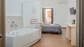 Un baño moderno con bañera, ducha y una cama con colcha gris.