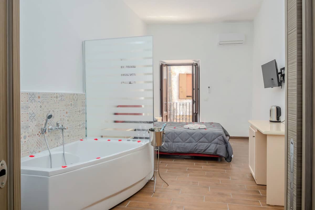 Un baño moderno con bañera, ducha y una cama con colcha gris.