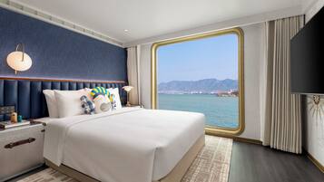 Une chambre d’hôtel avec un grand lit, une table de chevet, une lampe, une vue sur la mer et une grande fenêtre.