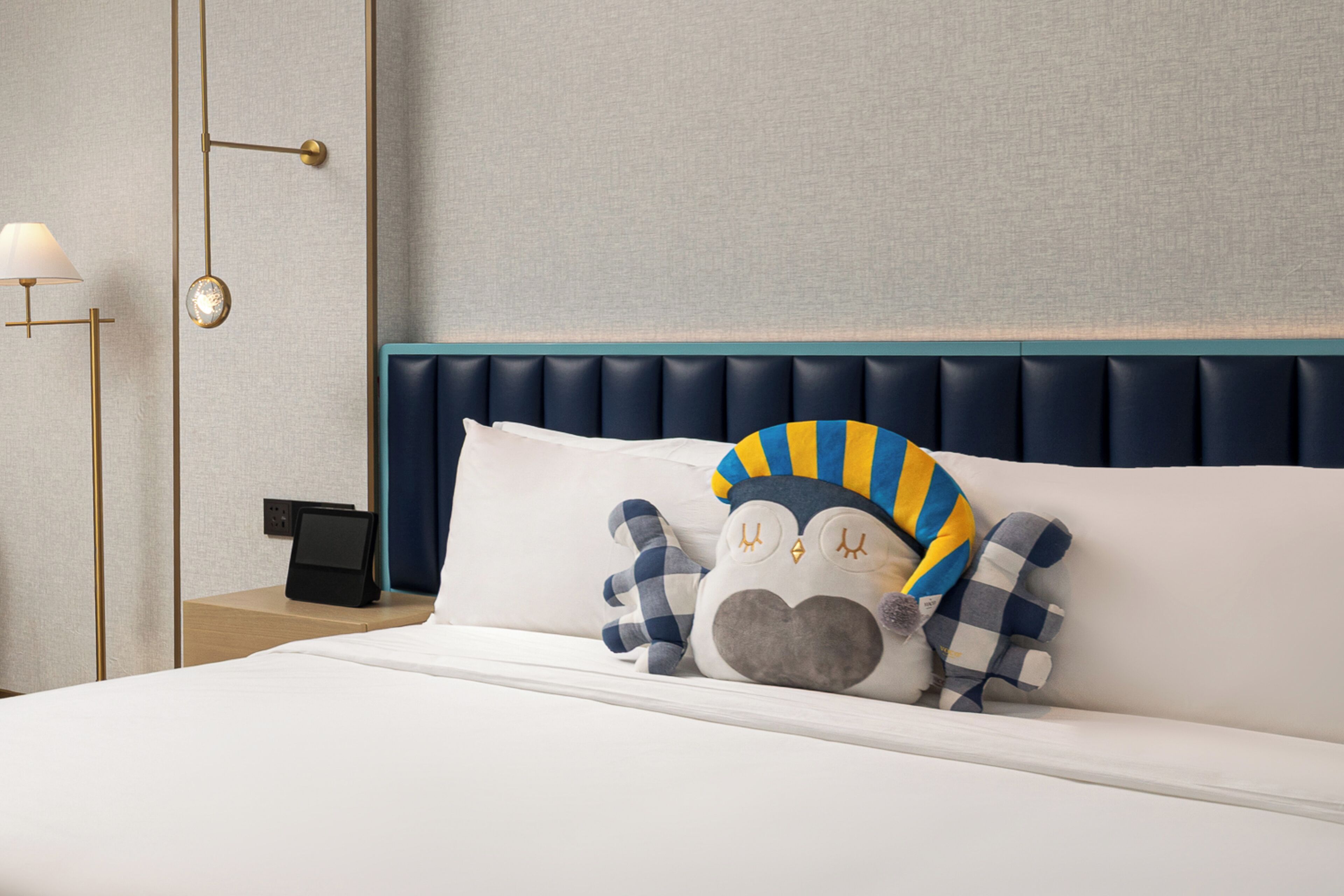 A neatly made bed with a plush owl pillow and a bedside lamp.