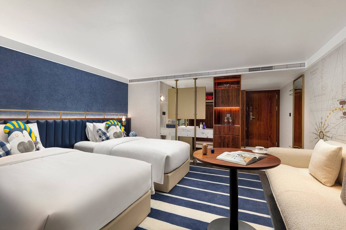 A hotel room with two beds, a sofa, a small table, and a map on the wall.