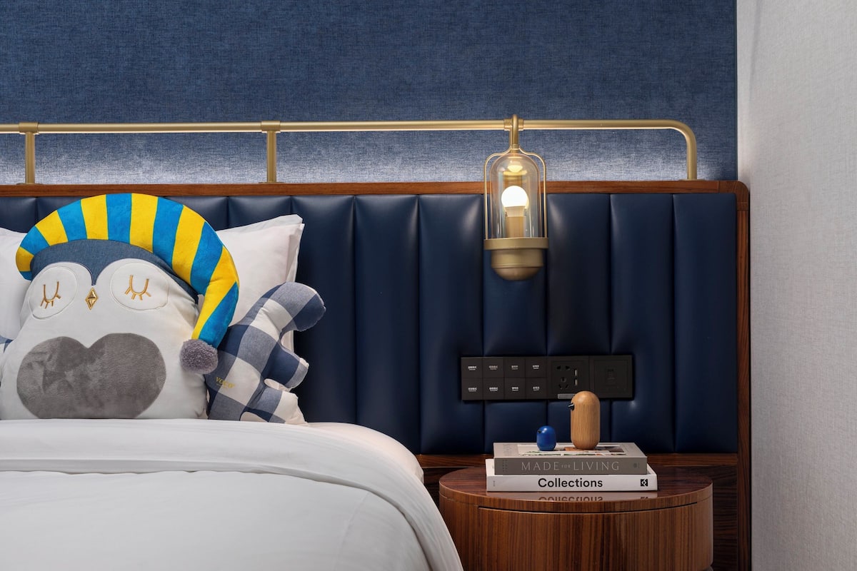 A bedroom with a dark blue headboard, a bedside table with books, and a lamp.