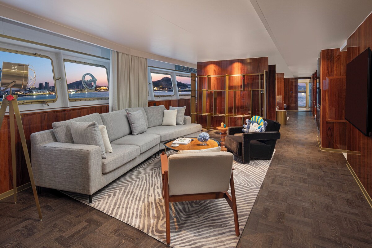 A modern living room with a sofa, armchairs, and a coffee table, featuring a large window with a city view.