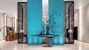 Un vestíbulo moderno con una fuente central, un mostrador de recepción y una pared decorativa con diseños geométricos.