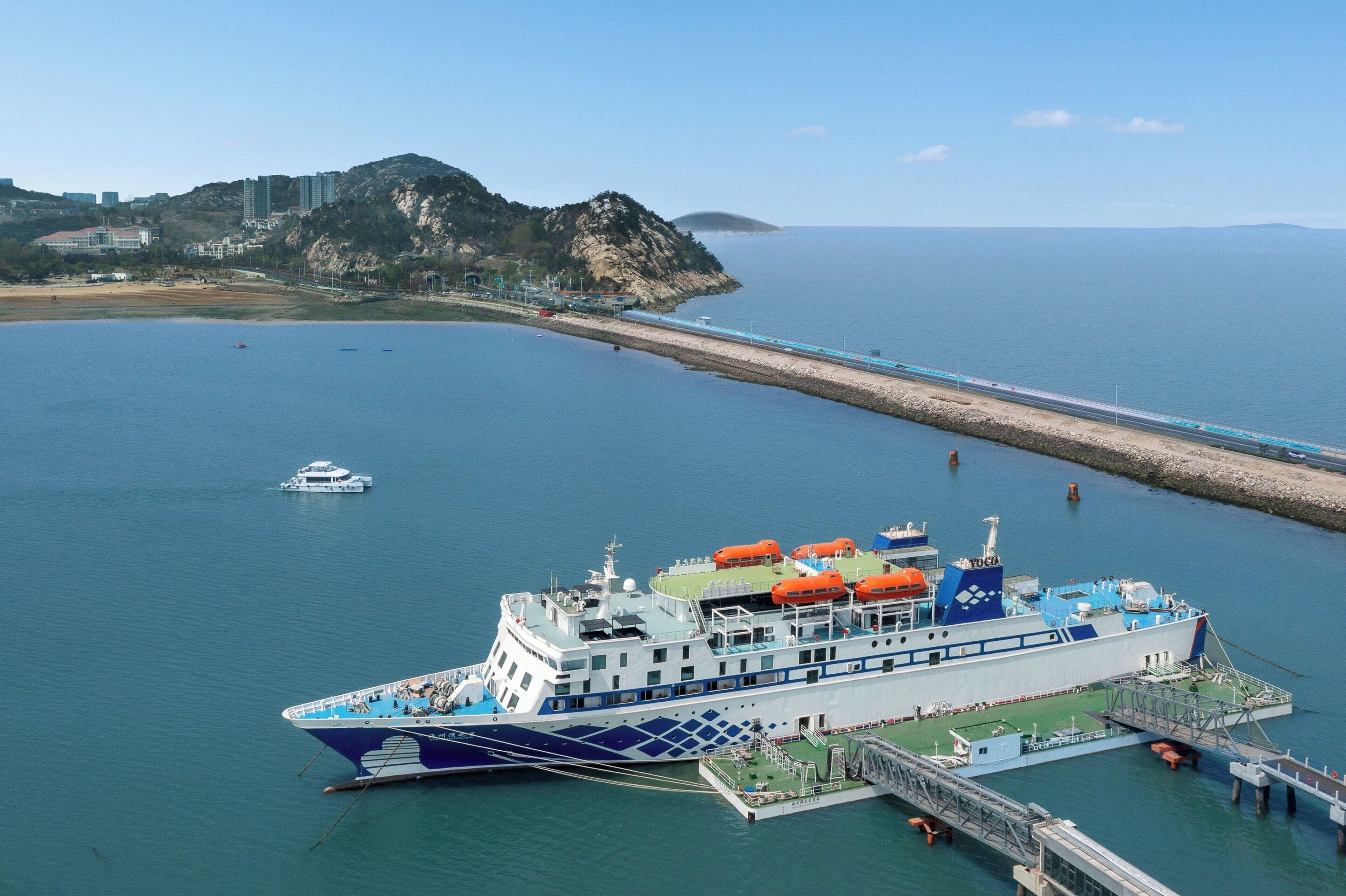 A large ferry docked at a pier with a mountainous backdrop and a clear sky.