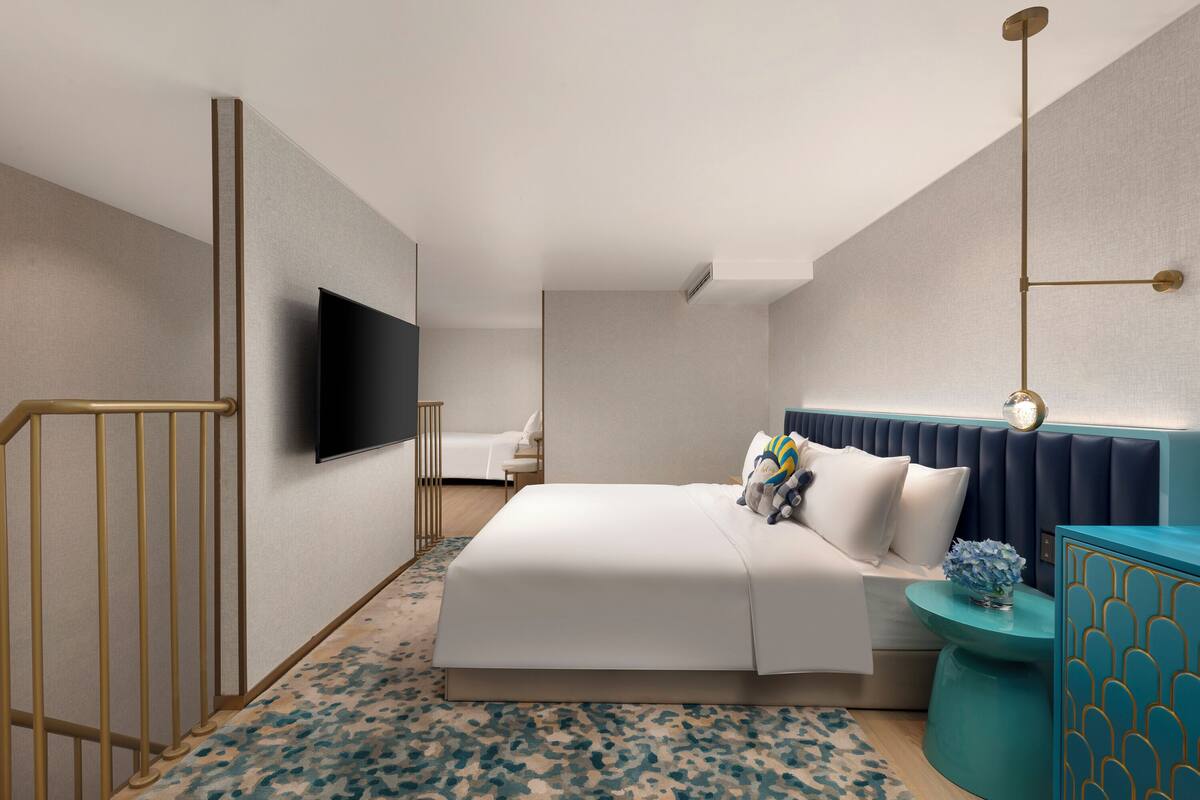 A modern hotel room with a large bed, a flat-screen TV, a bedside table with a vase, and a unique blue accent wall.