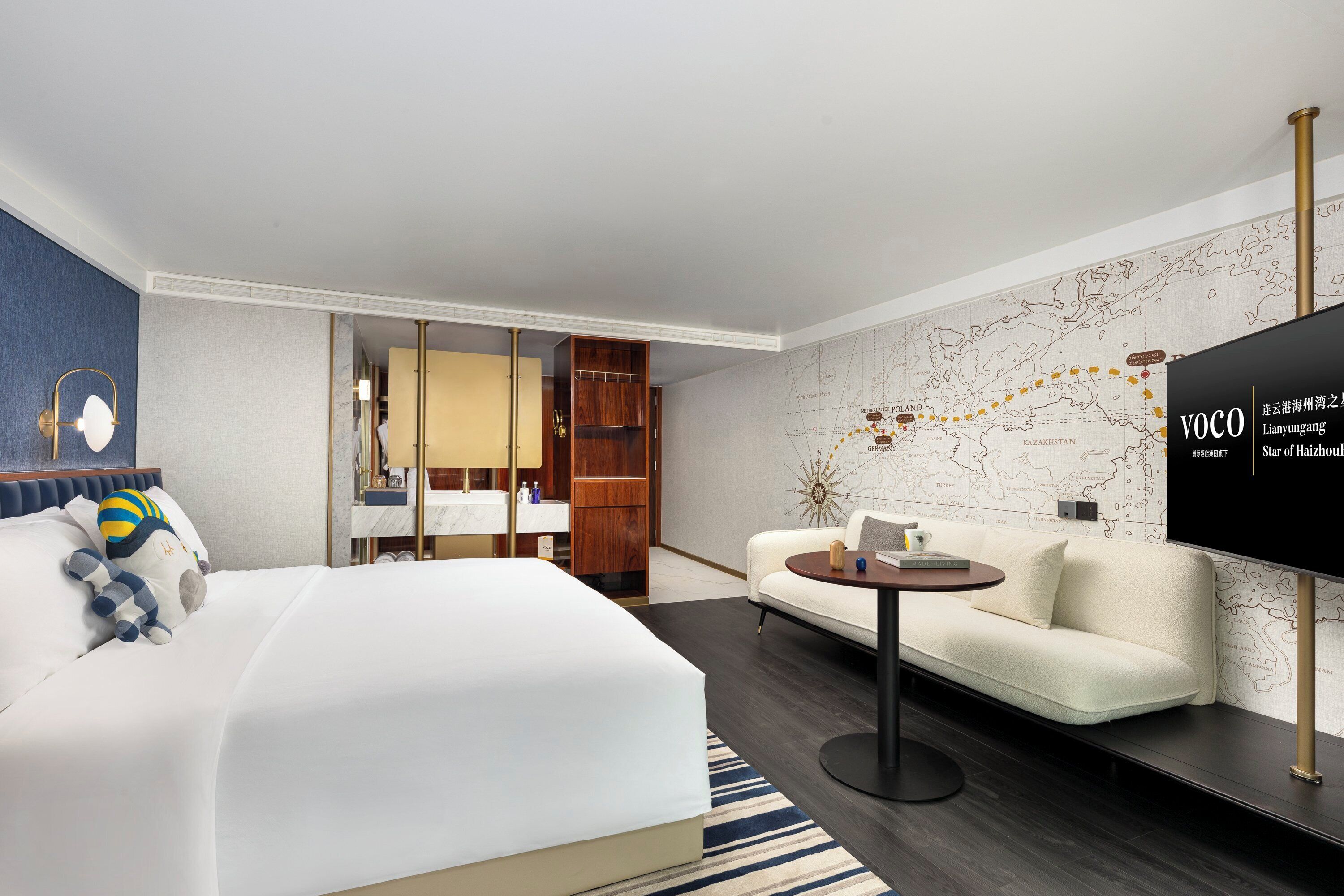 A modern hotel room with a large bed, a sofa, a small table, and a map on the wall.