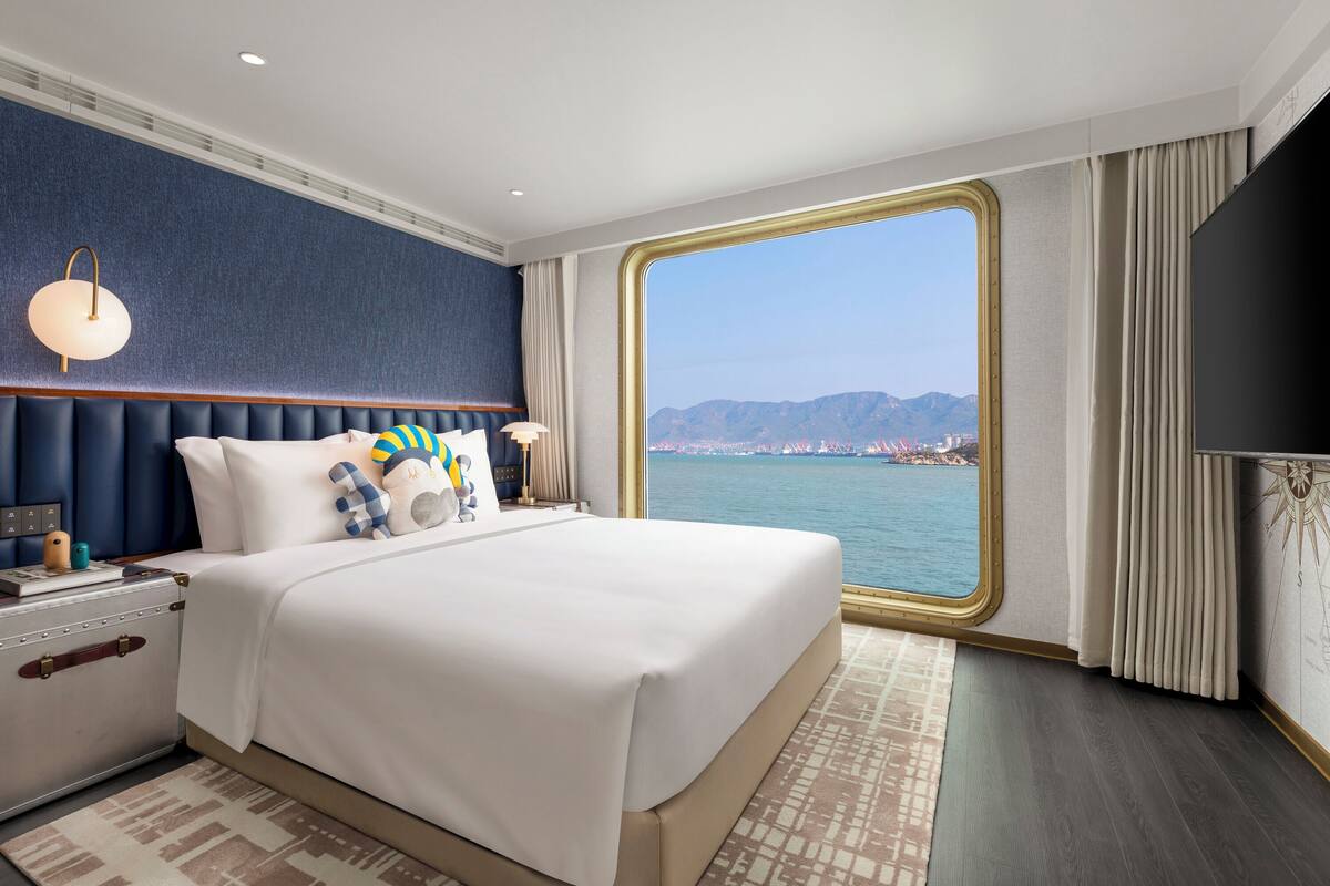 A spacious bedroom with a large bed, a nightstand, a suitcase, and a TV.