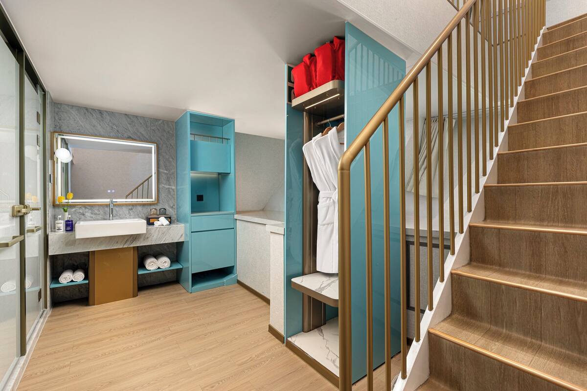 A modern bathroom with a marble sink, a mirror, and a wooden staircase.