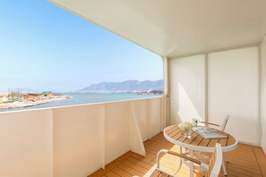A balcony with a wooden table and chairs, overlooking a body of water and distant mountains. - Voco Lianyungang Star Of Haizhoubay by IHG (Lianyungang)