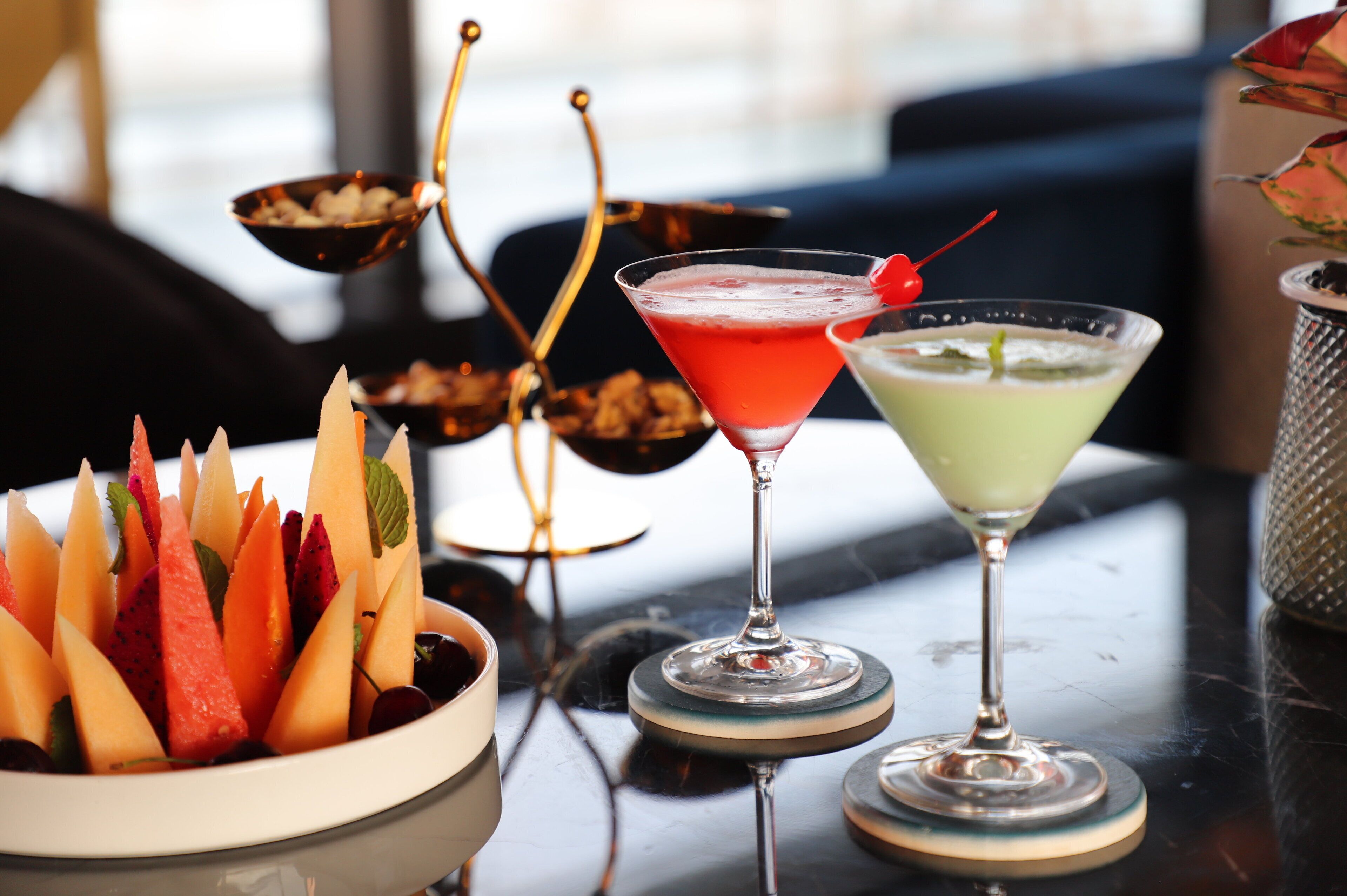 A table with a bowl of fruit and two martini glasses.