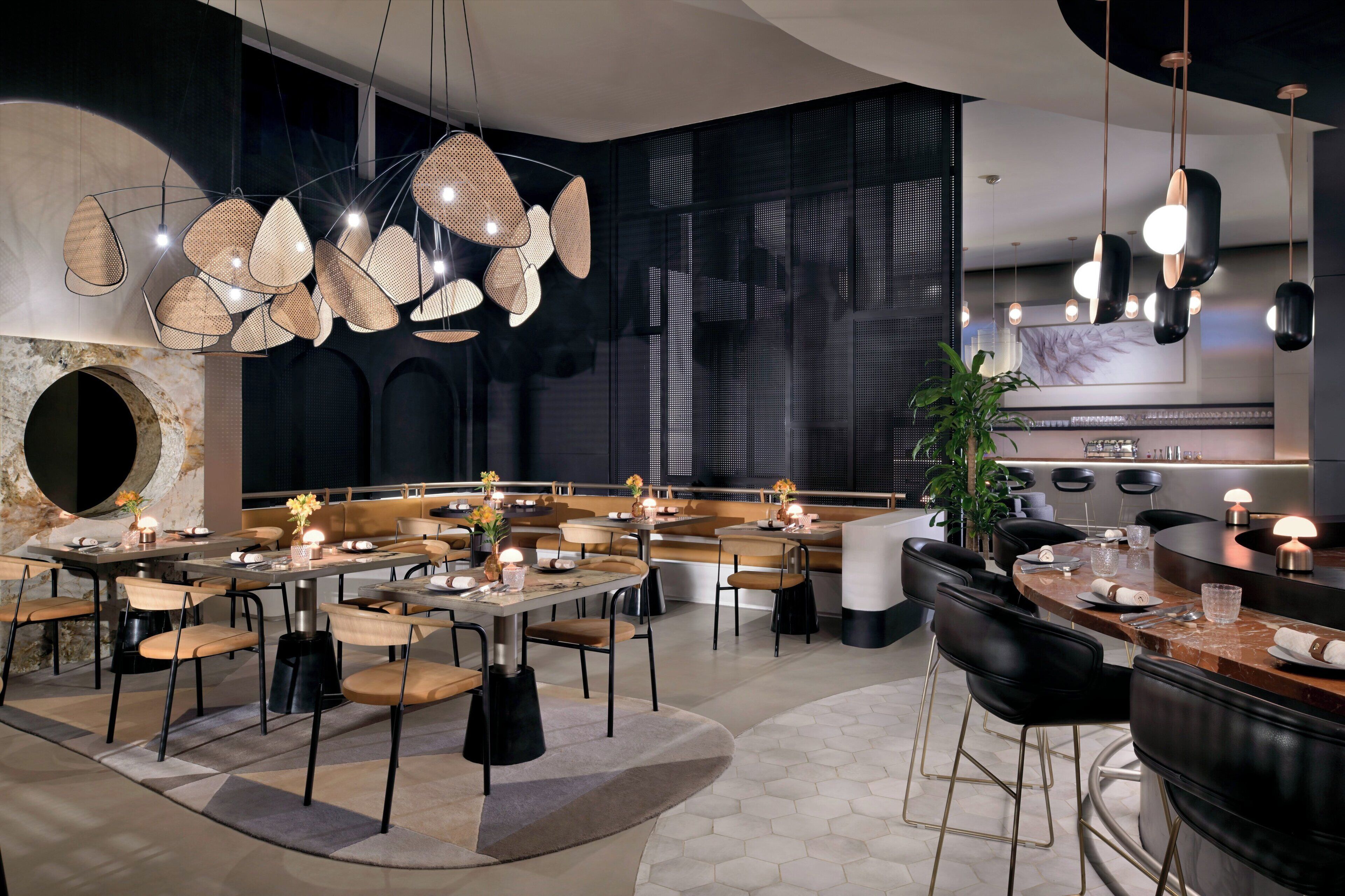 Un restaurante moderno con una zona de asientos central, una barra y una cocina visible al fondo.