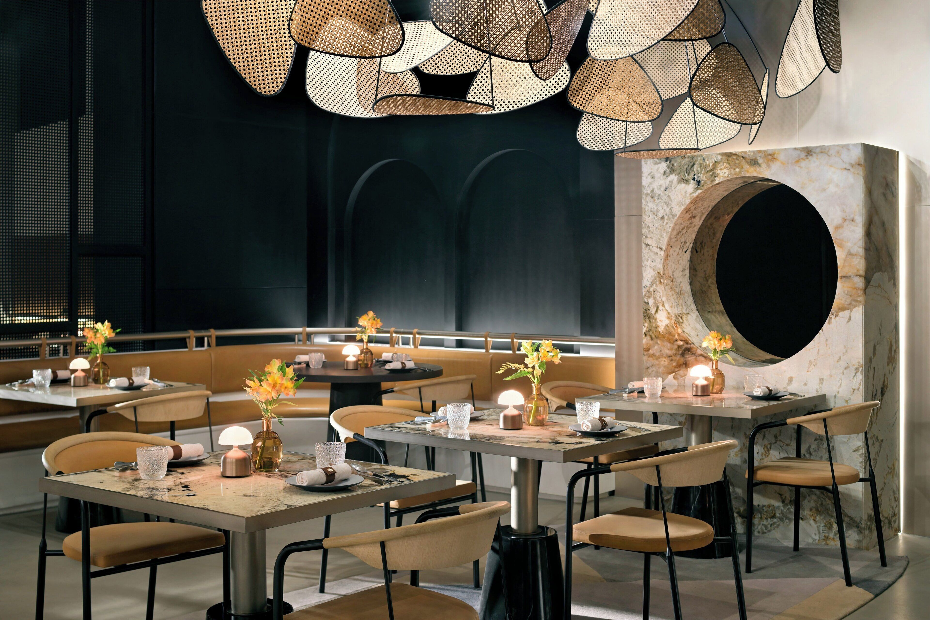 A modern restaurant with round tables, cushioned chairs, and decorative lighting.