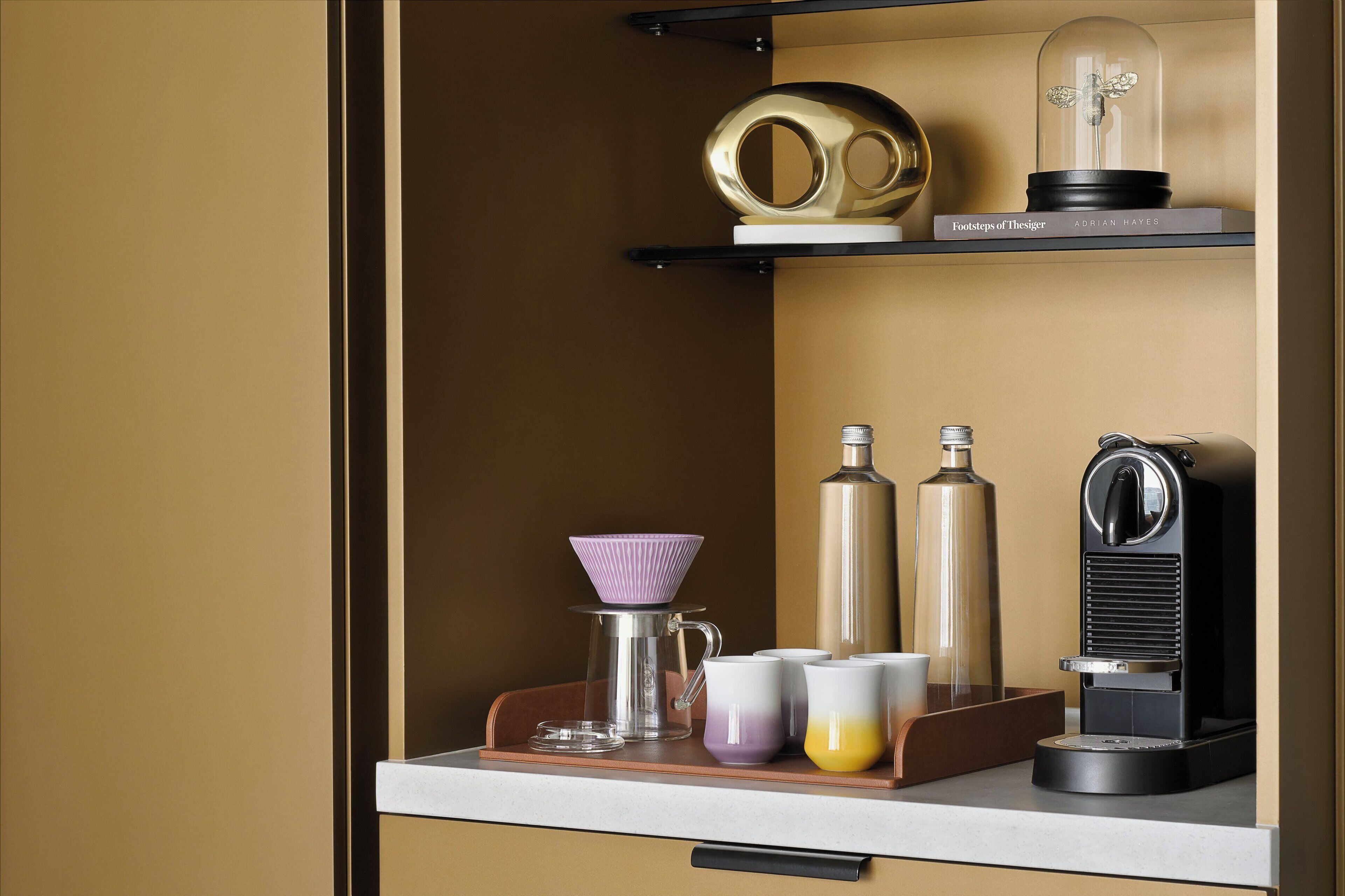 A coffee station with a coffee machine, a glass carafe, a thermos, and a book titled 'Footsteps of the Tiger'.