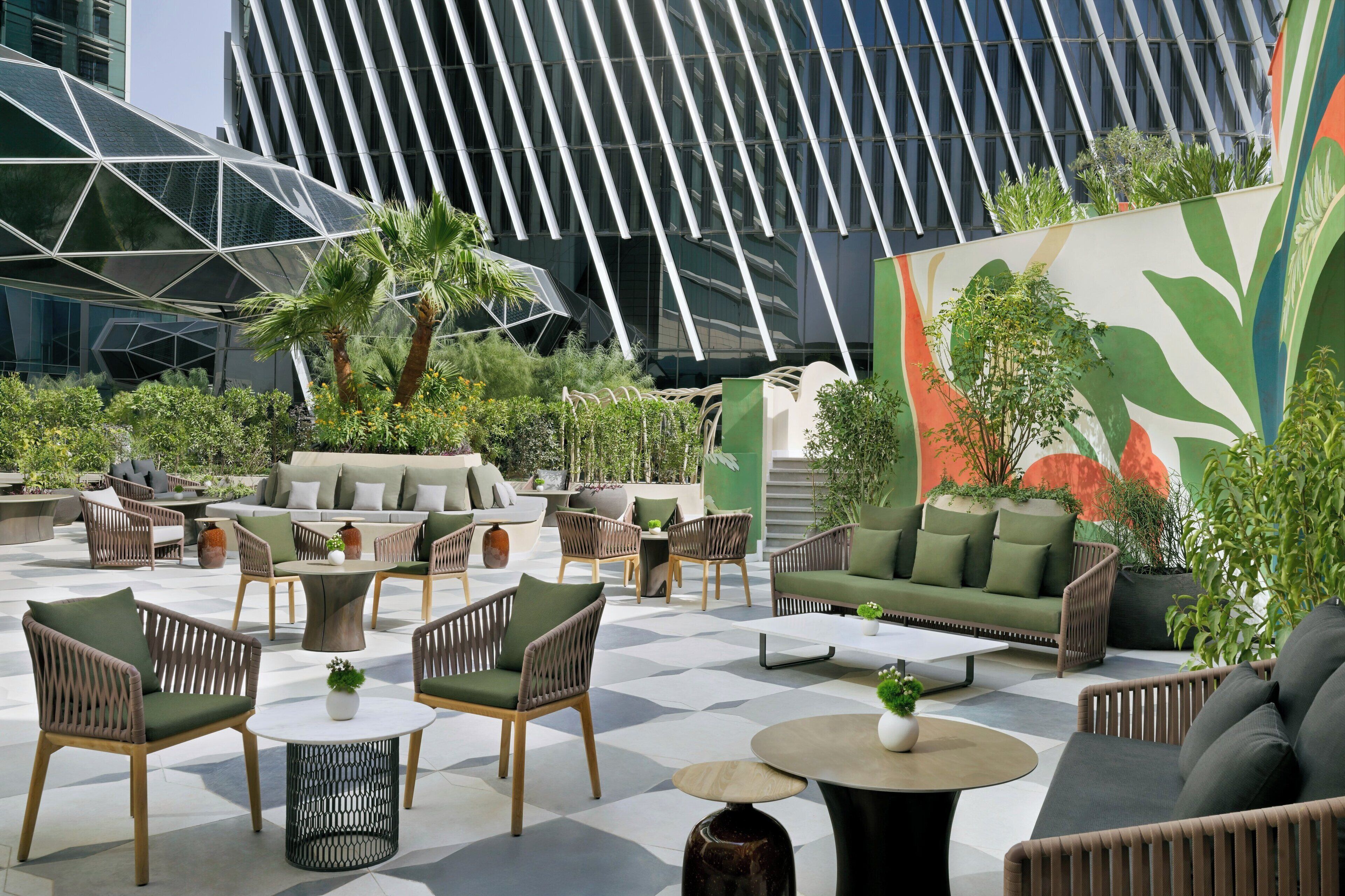 An outdoor seating area with modern furniture, surrounded by greenery and a large mural.