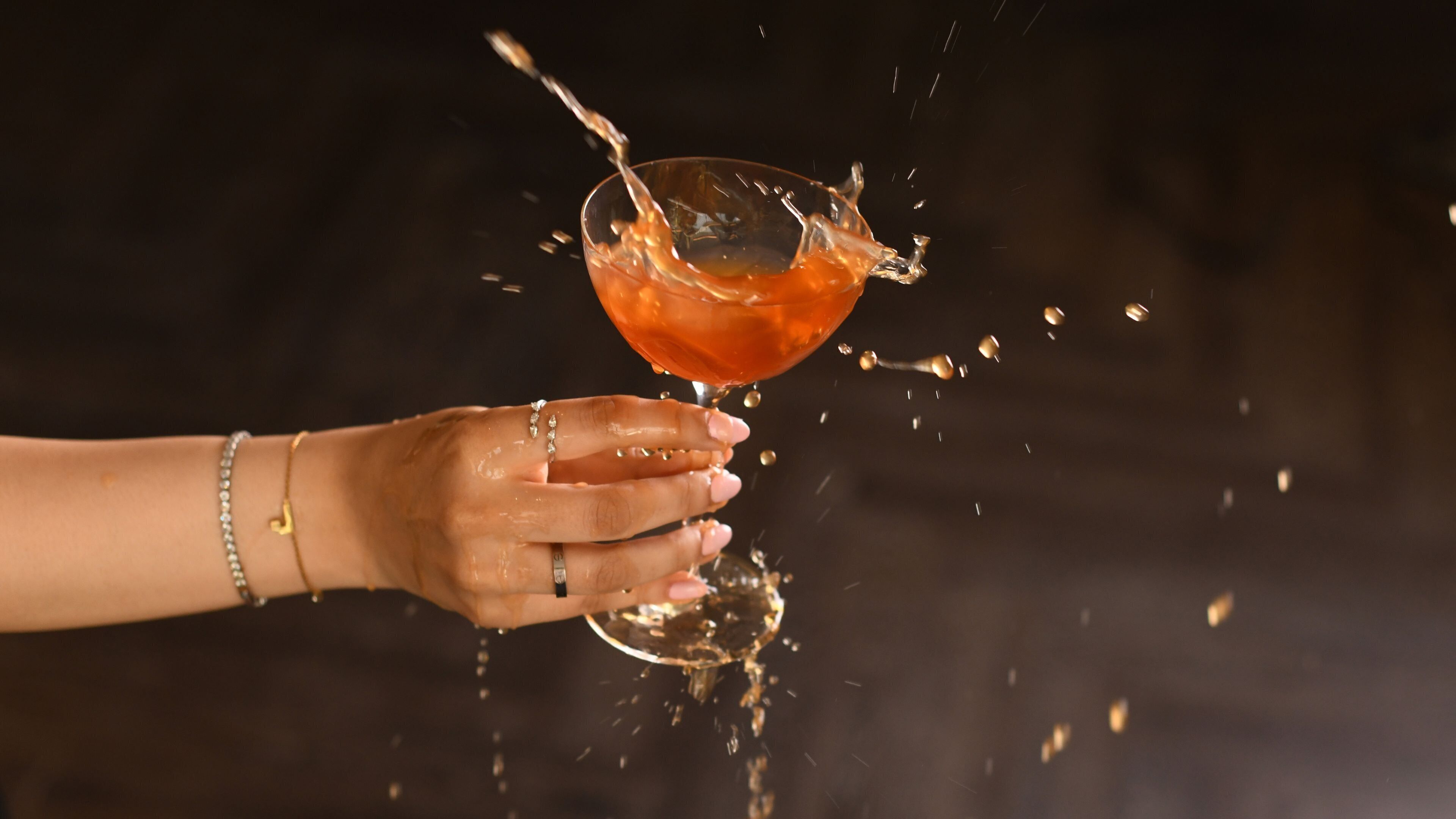 A hand holding a glass with a liquid being poured into it, creating a splash.
