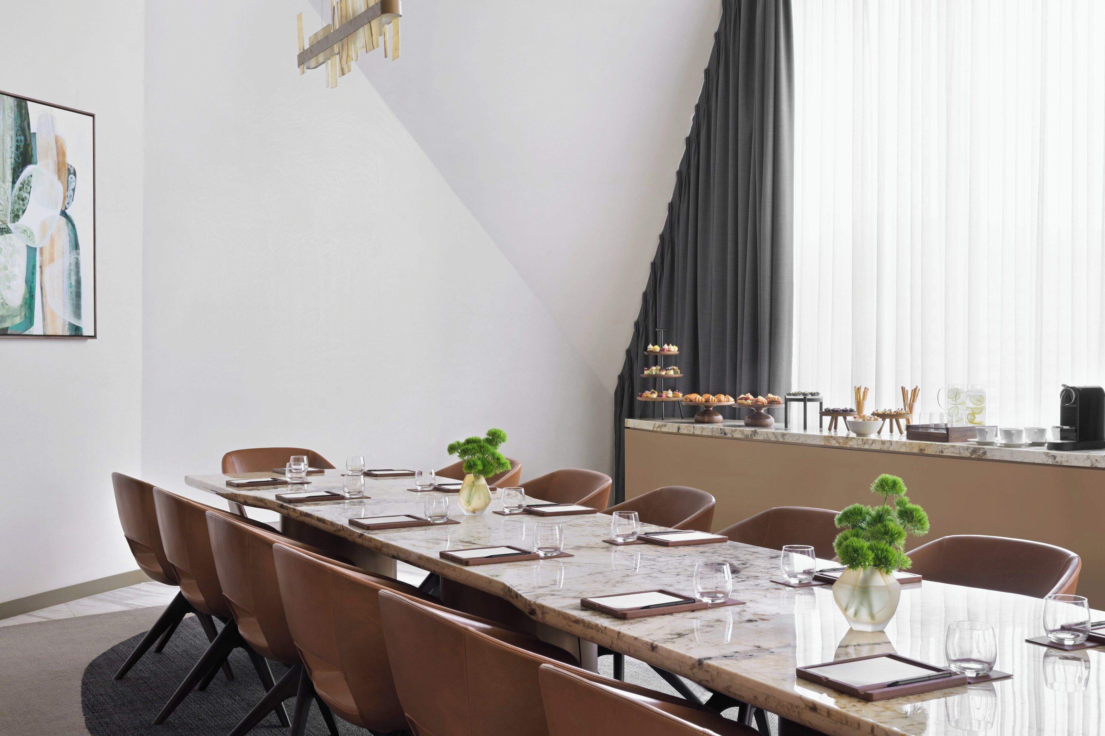 Un salón de conferencias con una larga mesa, sillas marrones y un jarrón con una planta.