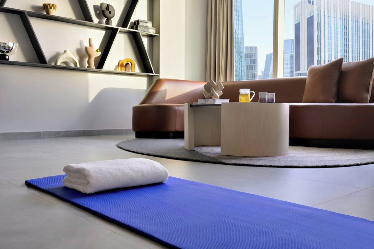 A modern living room with a blue exercise mat, a brown sofa, and a coffee table with a drink.