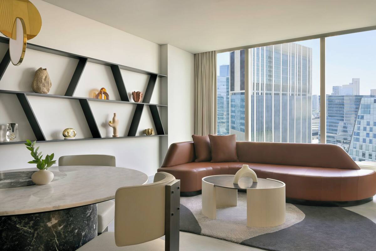 A modern living room with a round marble table, a leather sofa, and a city view through large windows.