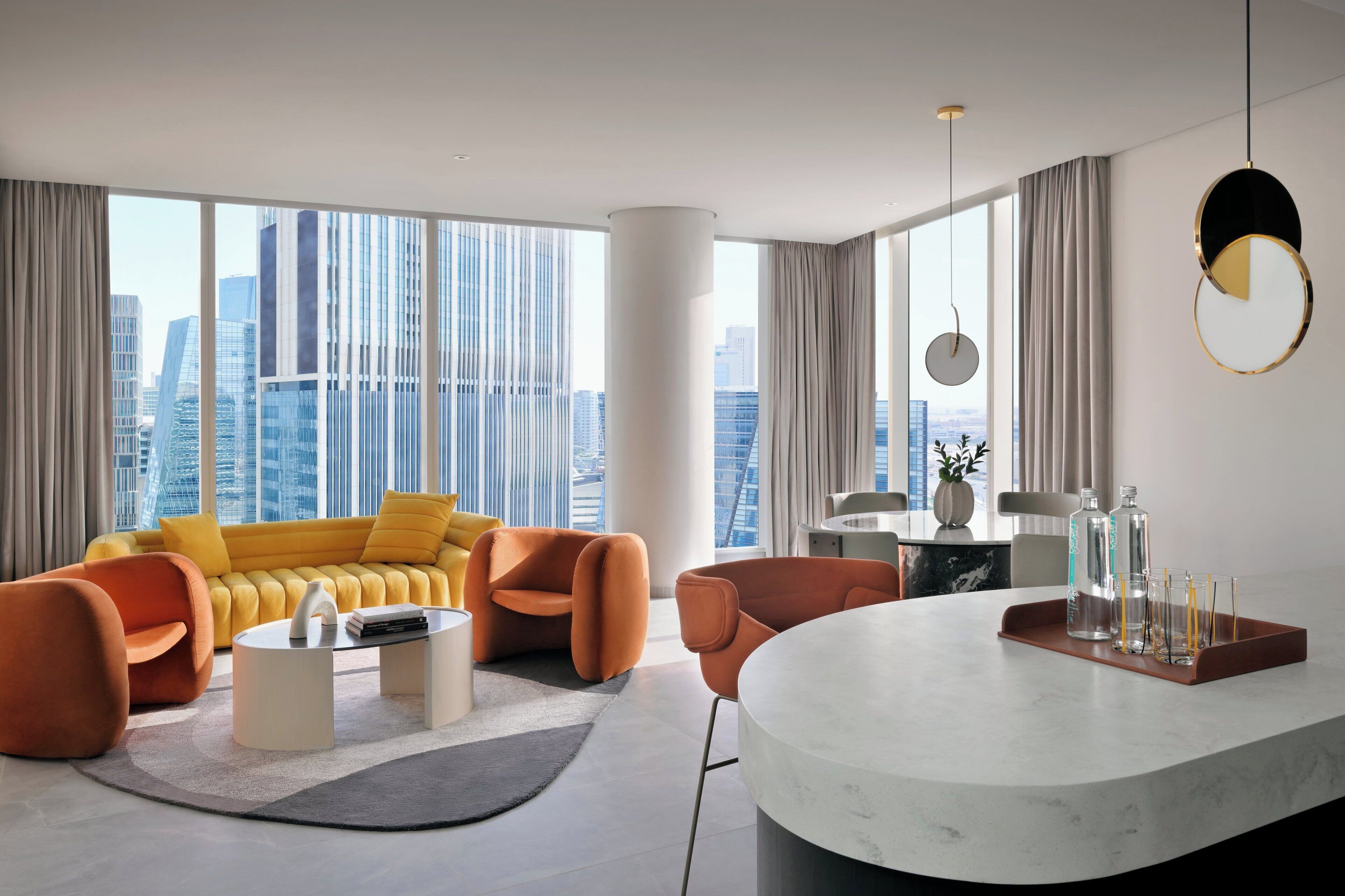 Una sala de estar moderna con un sofá amarillo, sillones naranjas, una mesa de centro de mármol y vistas a la ciudad a través de amplios ventanales.