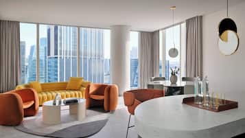 Una sala de estar moderna con un sofá amarillo, sillones naranjas, una mesa de centro de mármol y vistas a la ciudad a través de amplios ventanales.