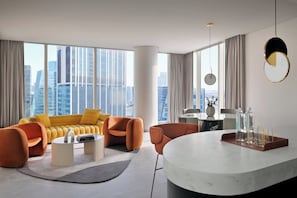 A modern living room with a yellow sofa, orange armchairs, a marble coffee table, and a city view through large windows.