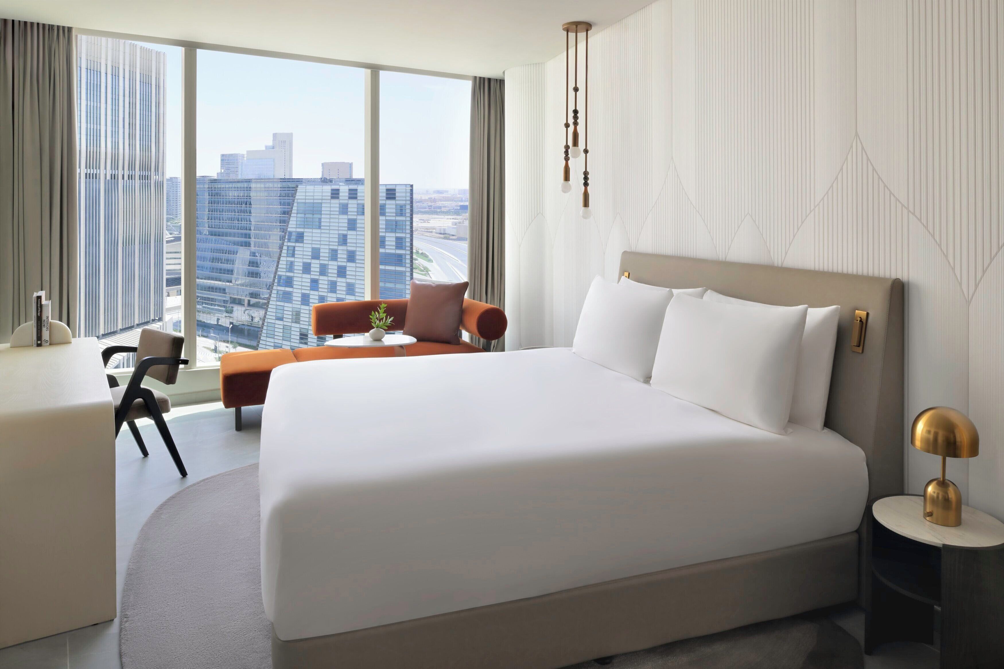 A modern hotel room with a large bed, a desk, and a view of the city skyline.